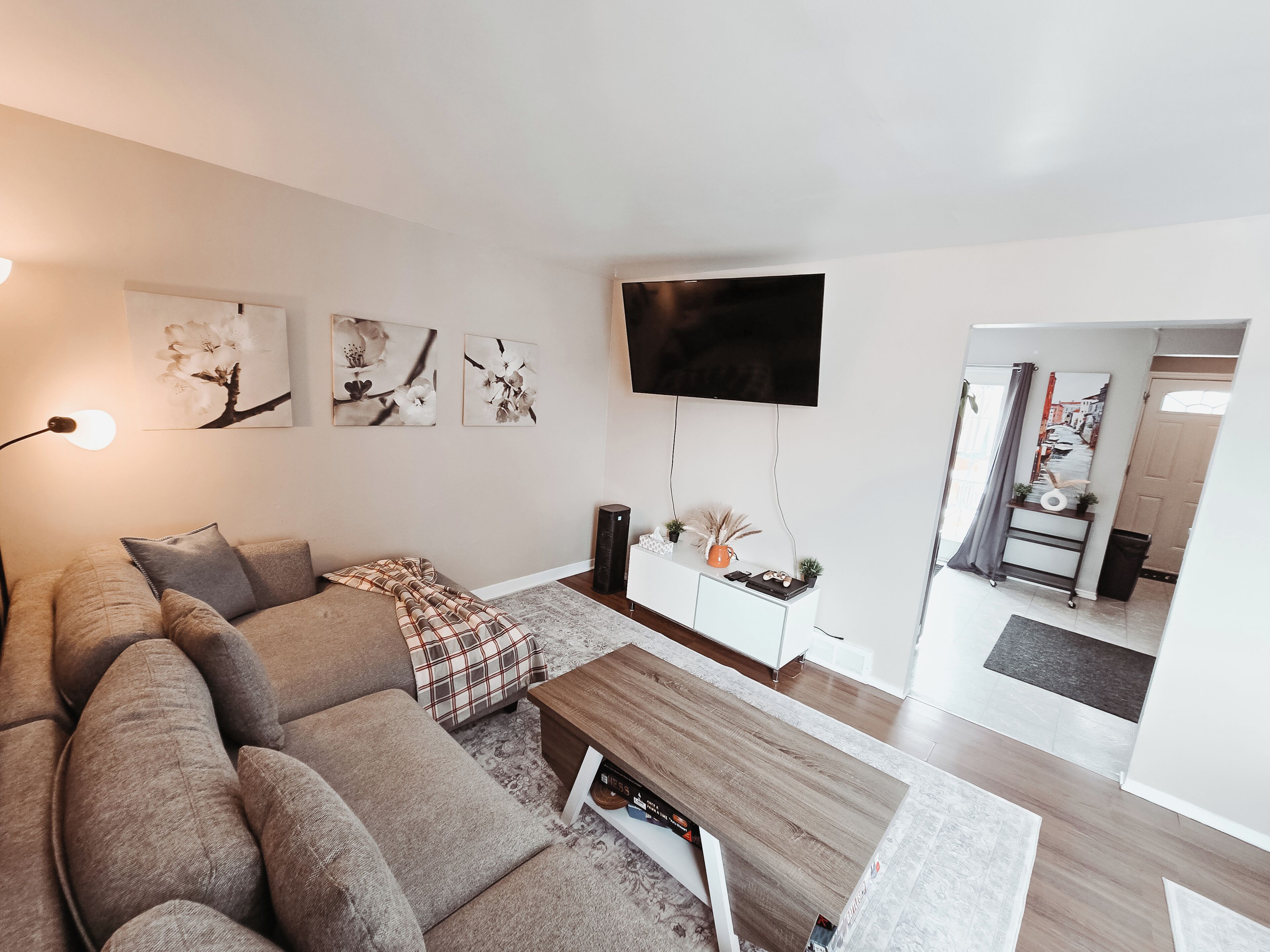 A modern living room with a sectional sofa, a coffee table, a flat-screen TV, artwork on the walls, and a small console table with decorative items.