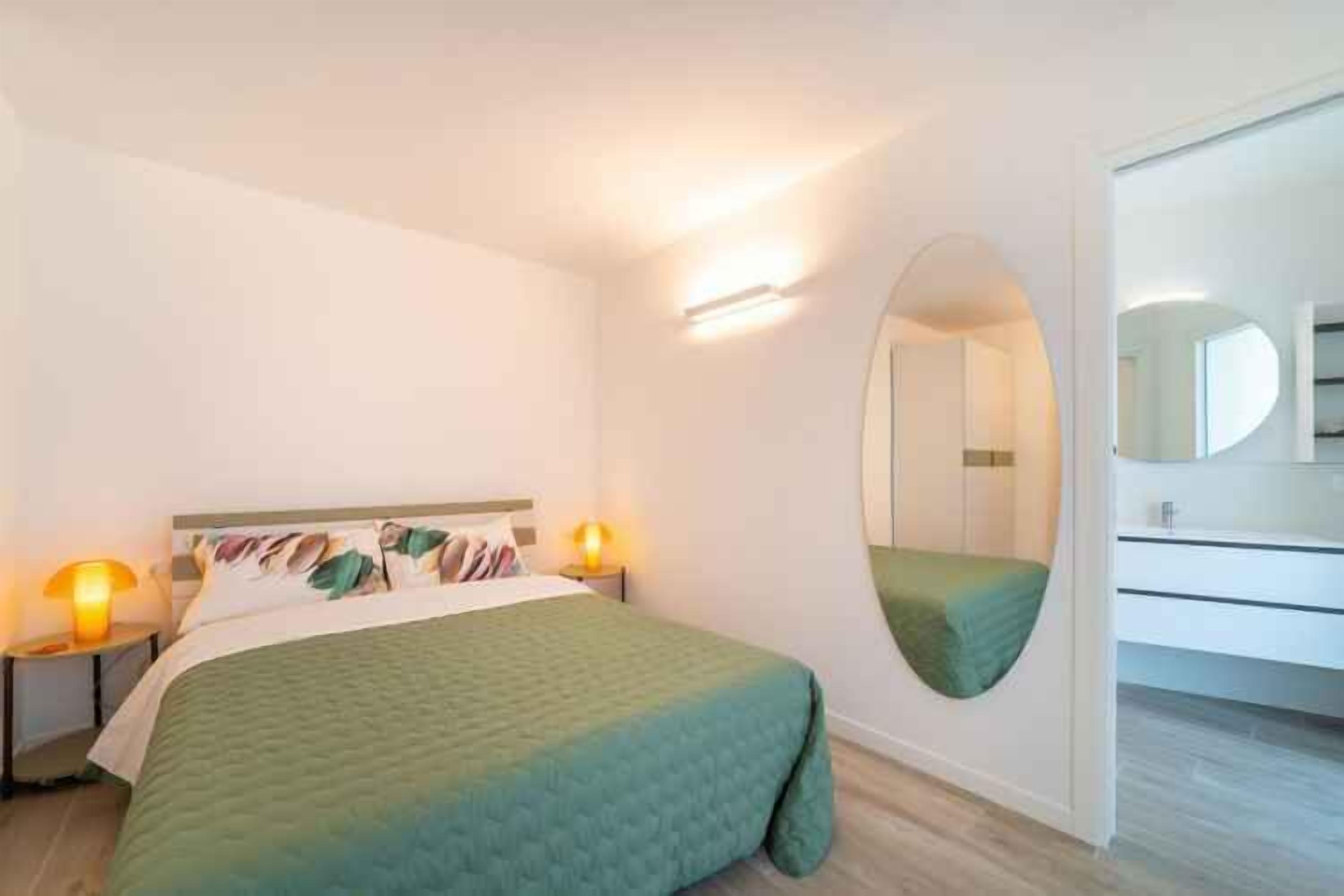 Una habitación de hotel moderna con cama, lámparas de noche, un espejo y un baño con inodoro y lavabo.