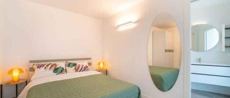Una habitación de hotel moderna con cama, lámparas de noche, un espejo y un baño con inodoro y lavabo.