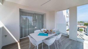 A balcony with a dining table, chairs, and a view of the city. - Holiday apartment with air conditioning and balcony (Lignano)