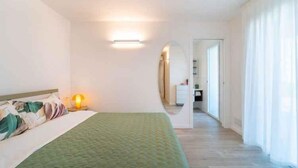 A hotel room with a bed, a nightstand, a lamp, and a view of the hallway. - Holiday apartment with air conditioning and balcony (Lignano)
