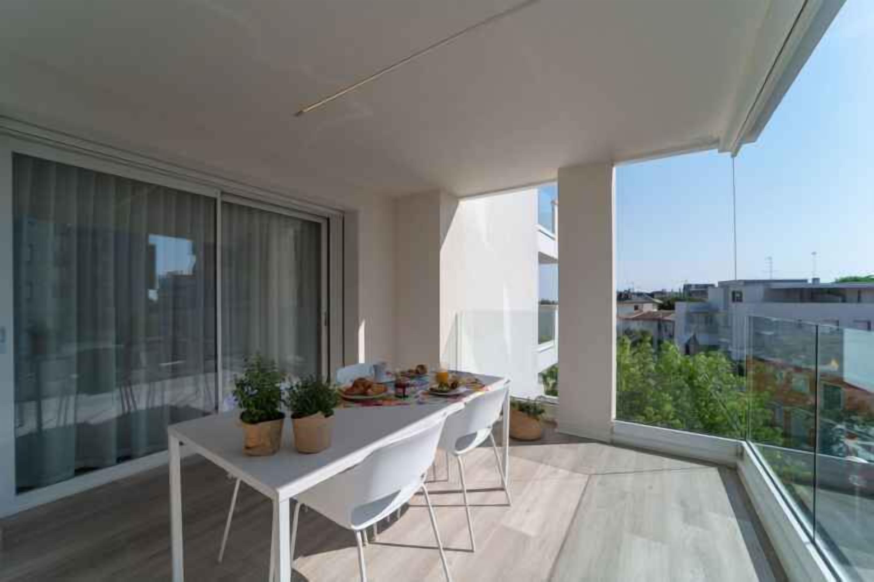 A balcony with a dining table set for two, potted plants, and a city view.
