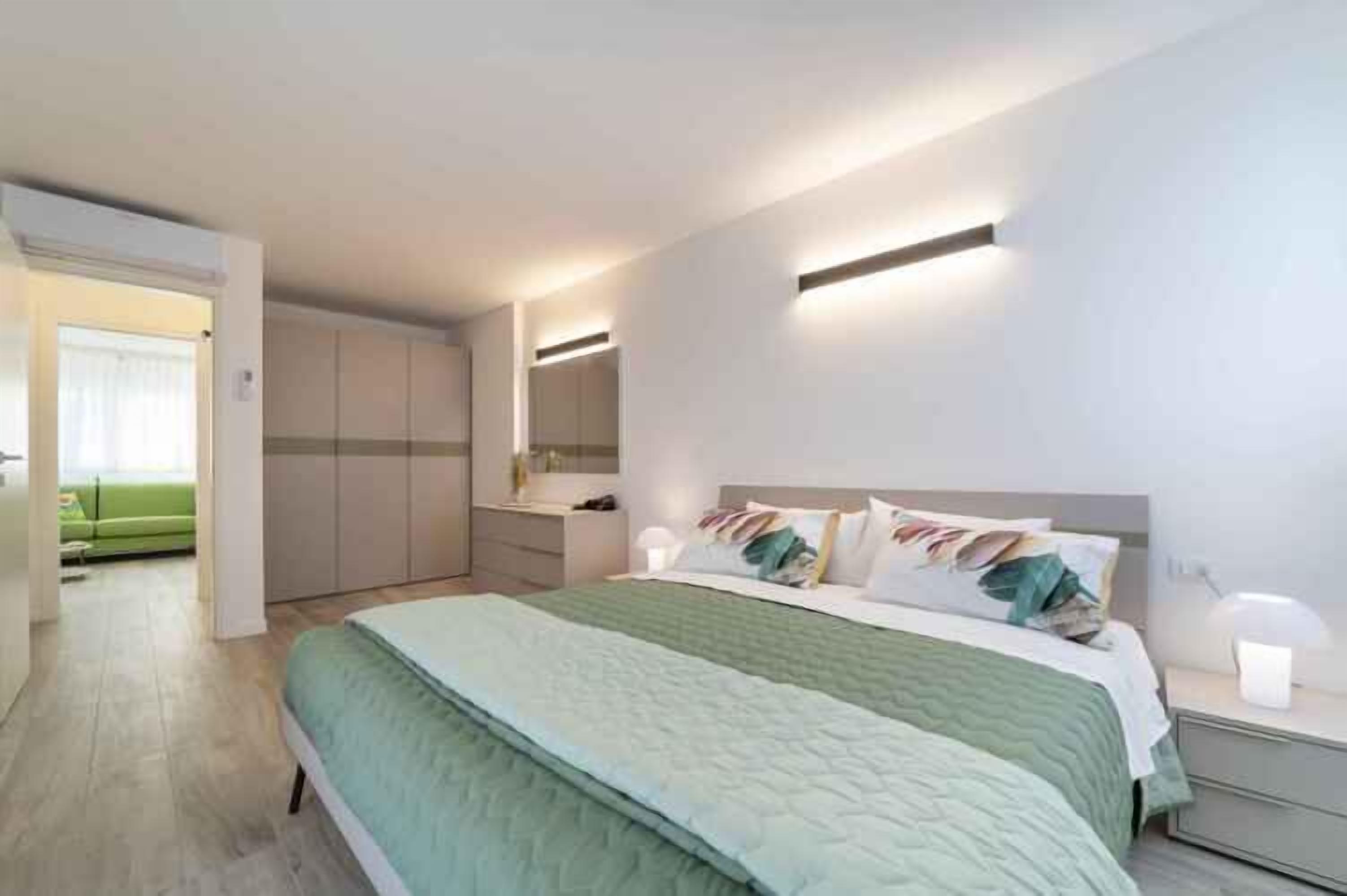 Een moderne slaapkamer met een groot bed, nachtkastjes, een kledingkast en een spiegel.