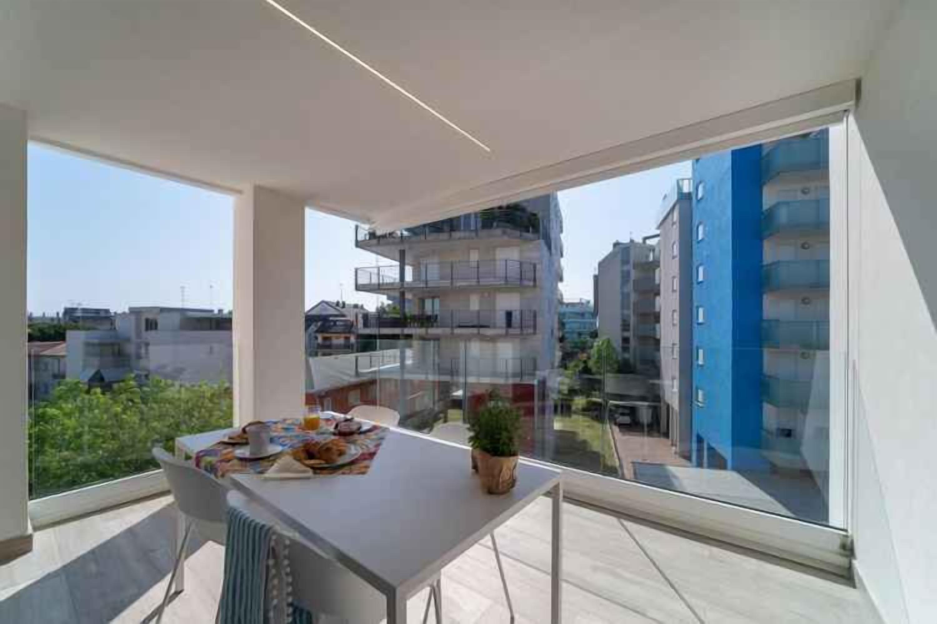 A modern apartment with a balcony, large windows, and a dining area with a table set for two.