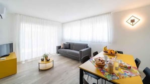Una sala de estar moderna con un sofá, una mesa de comedor con desayuno servido y un televisor sobre un mueble amarillo.