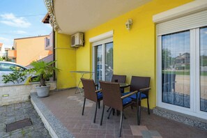 Un bâtiment jaune doté d’un patio aménagé avec des chaises en osier, une table et un pot de fleurs.