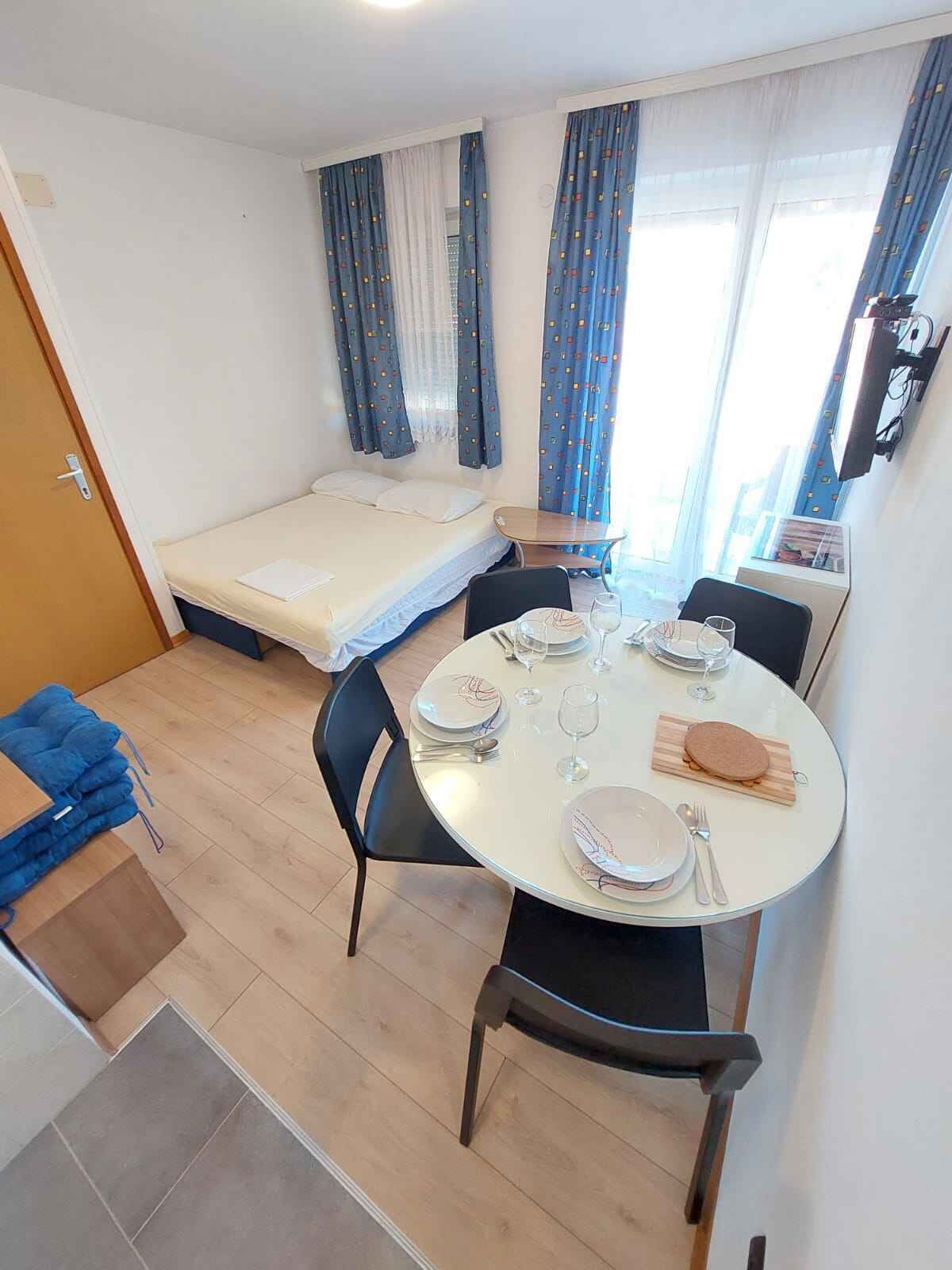 Une chambre d’hôtel compacte comprenant un lit, une petite table à manger pour deux personnes et un coin cuisine.