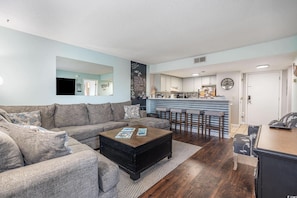 A living room with a sofa, coffee table, and a kitchen area with a bar counter.