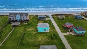 Vue aérienne d’un quartier résidentiel situé sur la côte, avec des maisons et une route menant à la plage.