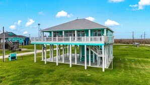 Une maison à deux étages avec un balcon, une véranda et une cour gazonnée.