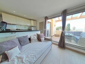 A modern living room with a sofa, a dining table, and a view of the outdoors. - Appartement 2 piéces  4 couchages ULYSSE PORT LEUCATE NATURISME (PORT LEUCATE NATURISME)