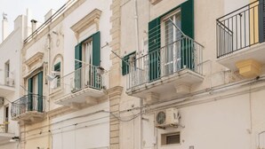 Een rij gebouwen met balkons, waarvan sommige groene luiken hebben, en een zichtbare airconditioning.