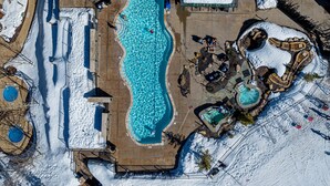Vista aèria d'un complex turístic amb una gran piscina, diverses zones de relaxació i un paisatge cobert de neu.