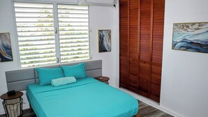 A bedroom with a bed, a bedside table, a window with blinds, and a wooden wardrobe. - Spacious 6-bedroom villa in gorgeous Luquillo with WiFi, AC (Luquillo)