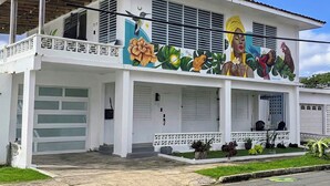 A two-story building with a balcony, a mural with tropical and floral designs, and a garage. - Spacious 6-bedroom villa in gorgeous Luquillo with WiFi, AC (Luquillo)