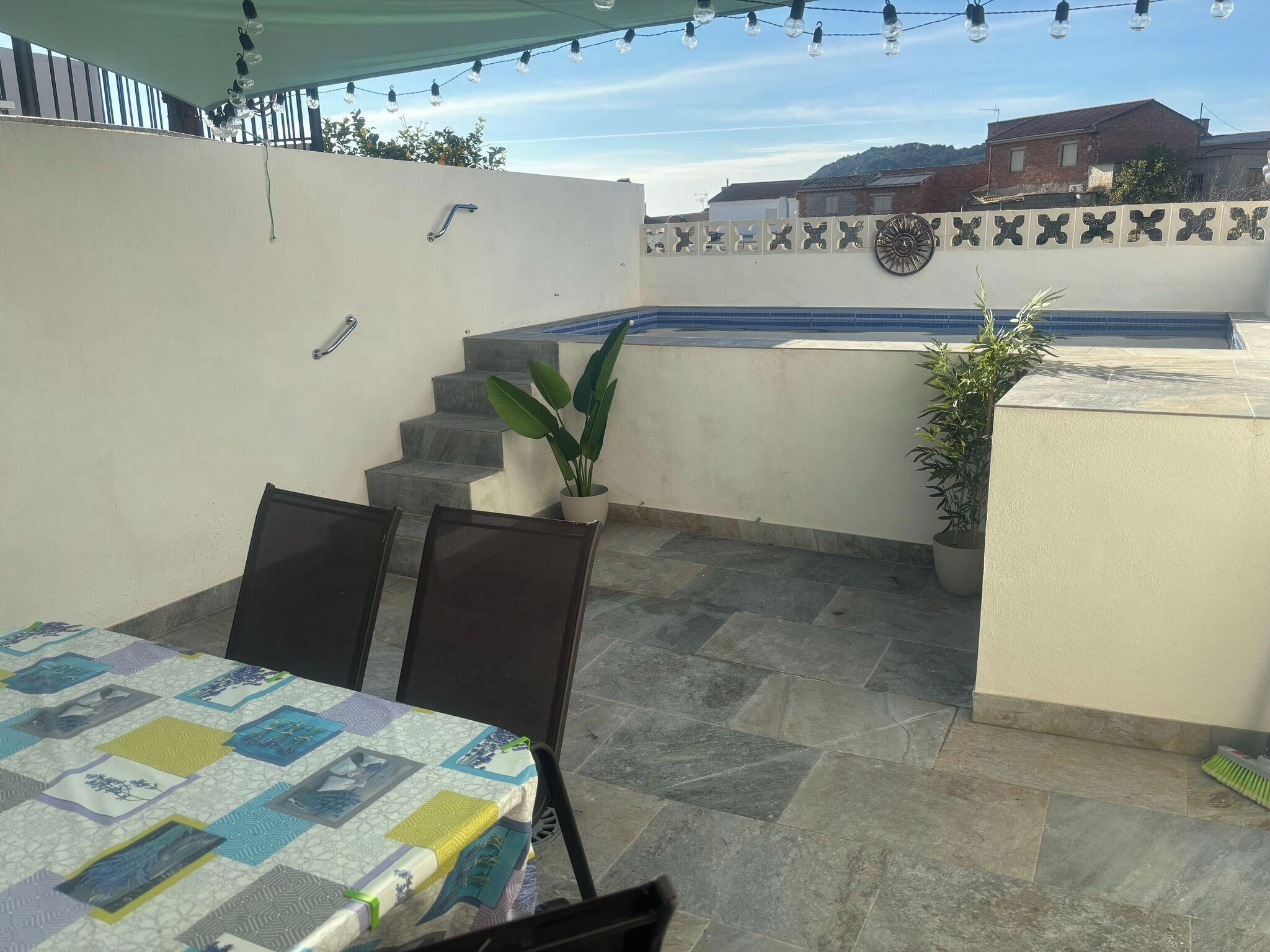 Un patio con mesa y sillas, una planta en maceta y una piscina al fondo.