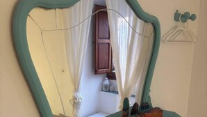 A mirror with a teal frame mounted on a wall, reflecting a room with a window, curtains, and a shelf with decorative items. - Casasona, Alcaudete,jaen,housesleeps4- Pool-patio (Alcaudete)