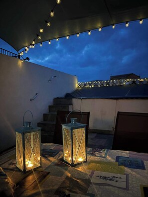 Une terrasse sur le toit, décorée de guirlandes lumineuses, de deux lanternes et d’un tapis à motifs.