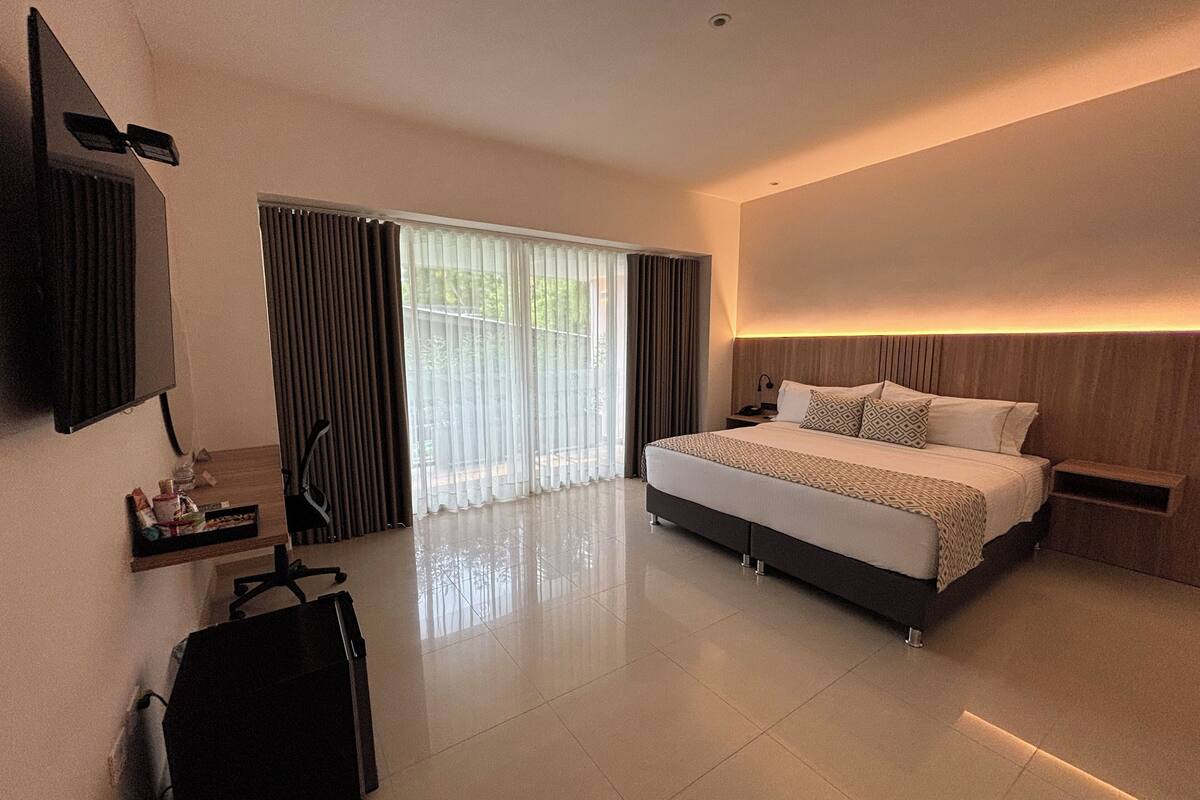 Een moderne hotelkamer met een groot bed, een bureau, een stoel en een aan de muur bevestigde televisie.