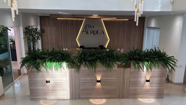 Una recepción con un cartel que dice "CASA AURORA", flanqueada por paneles de madera e iluminada por lámparas colgantes.