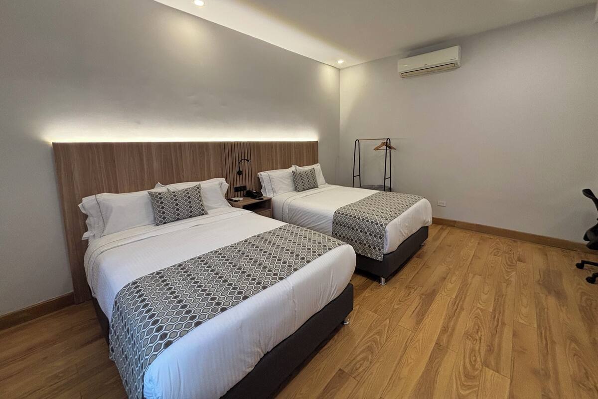 Een moderne hotelkamer met twee bedden, een houten hoofdbord, een nachtkastje met een lamp en een airconditioner aan de muur.