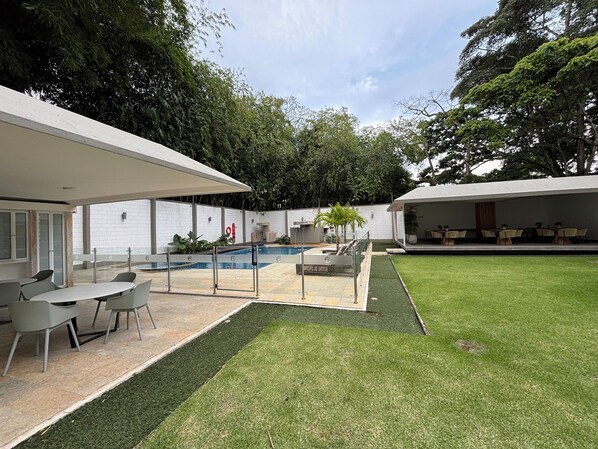 Un espacio exterior moderno con piscina, mobiliario y porche cubierto.