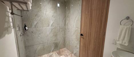 Un baño moderno con ducha de vidrio, paredes de mármol, un mueble de madera y un lavamanos blanco.