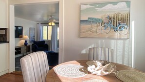 Un coin repas avec une table ronde, des chaises à rayures et un tableau sur le thème de la plage.
