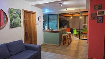 Una sala de estar con un sofá azul, una puerta de madera y una zona de cocina con barra y sillas coloridas.
