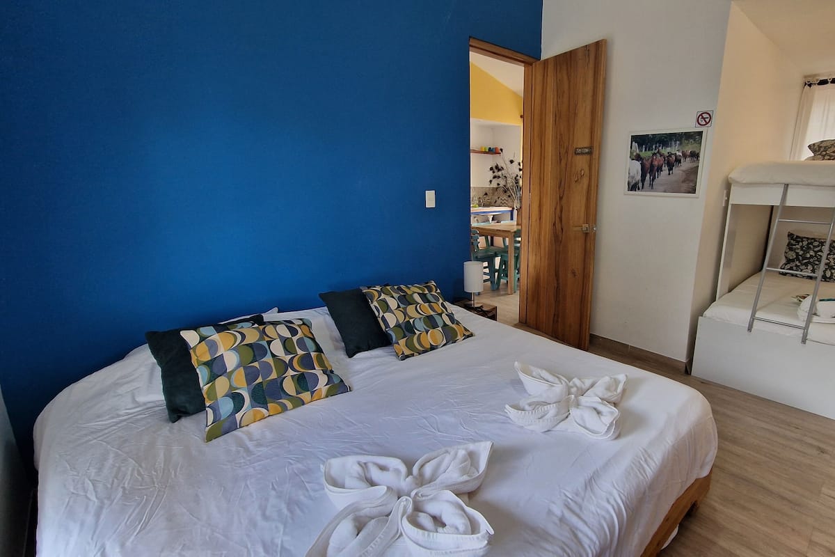 A hotel room with a large bed, a bunk bed, and a wooden floor.