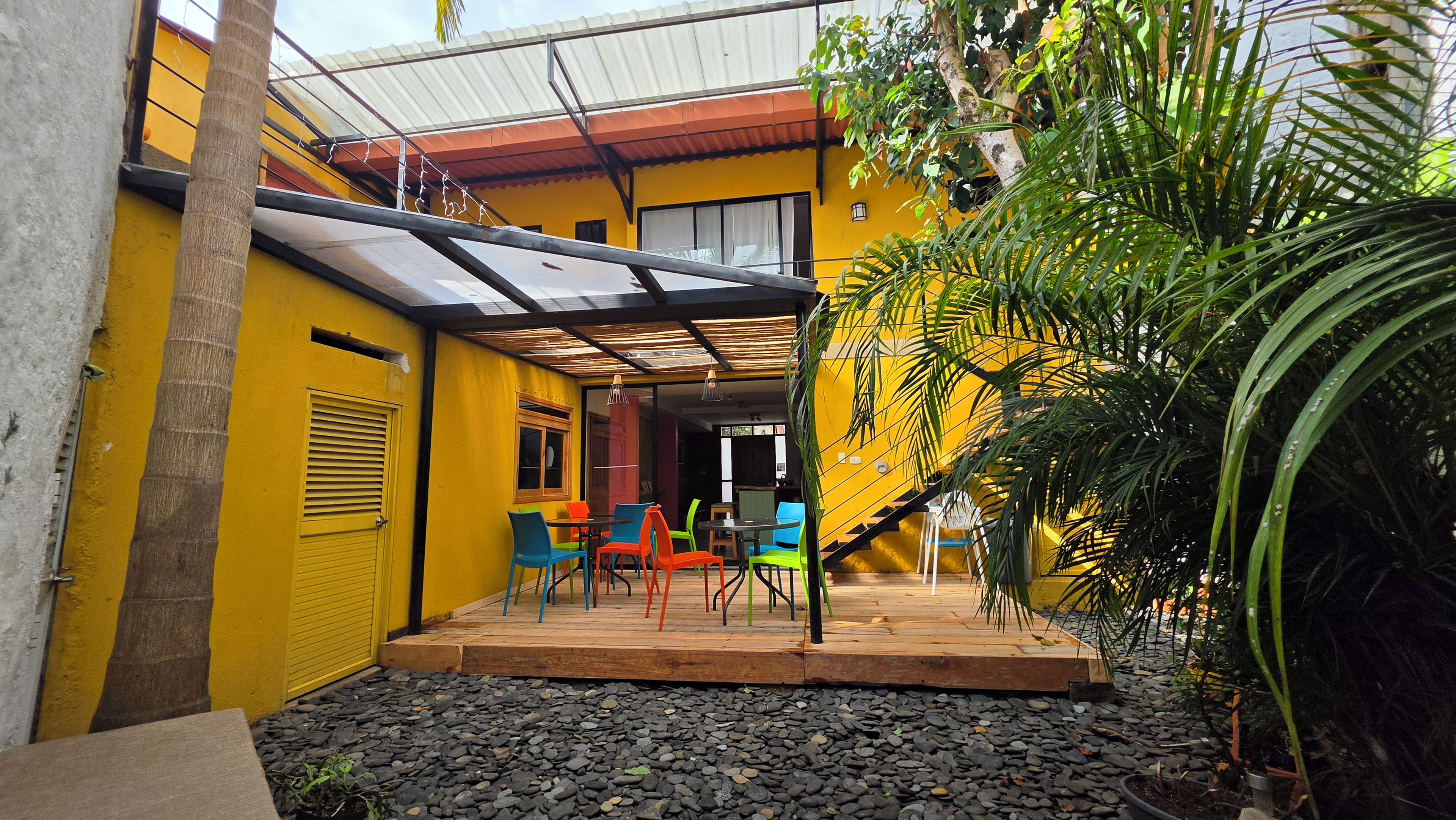 Un edificio amarillo con un patio cubierto, asientos al aire libre y una escalera que lleva a un nivel superior.