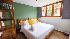 A bedroom with a wooden bed frame, white bedding, and a view of greenery through a window.