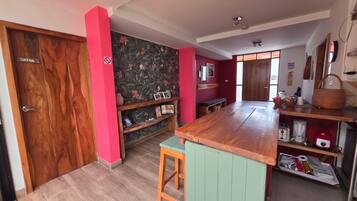 Una cocina con una puerta de madera identificada con 'SIRENA', una pared de acento roja y una isla de madera con un taburete verde.