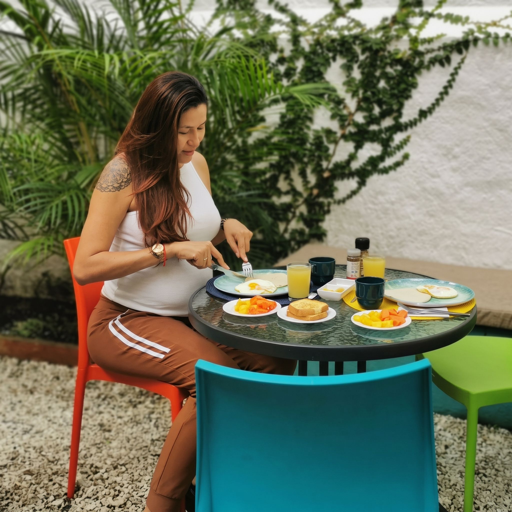 Una persona cenando en una mesa al aire libre con platos de comida, un vaso de jugo y una botella de salsa.