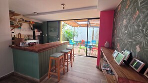 A kitchen with a bar area, wooden stools, and a view of the outdoor patio with colorful chairs. - Hotel La Caracola Salento (Salento)