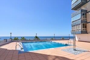 A rooftop pool with a view of the ocean, surrounded by a balcony with railings and potted plants.
