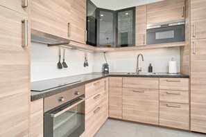 A modern kitchen with wooden cabinets, a stainless steel oven, a microwave, and a glass-fronted cabinet.