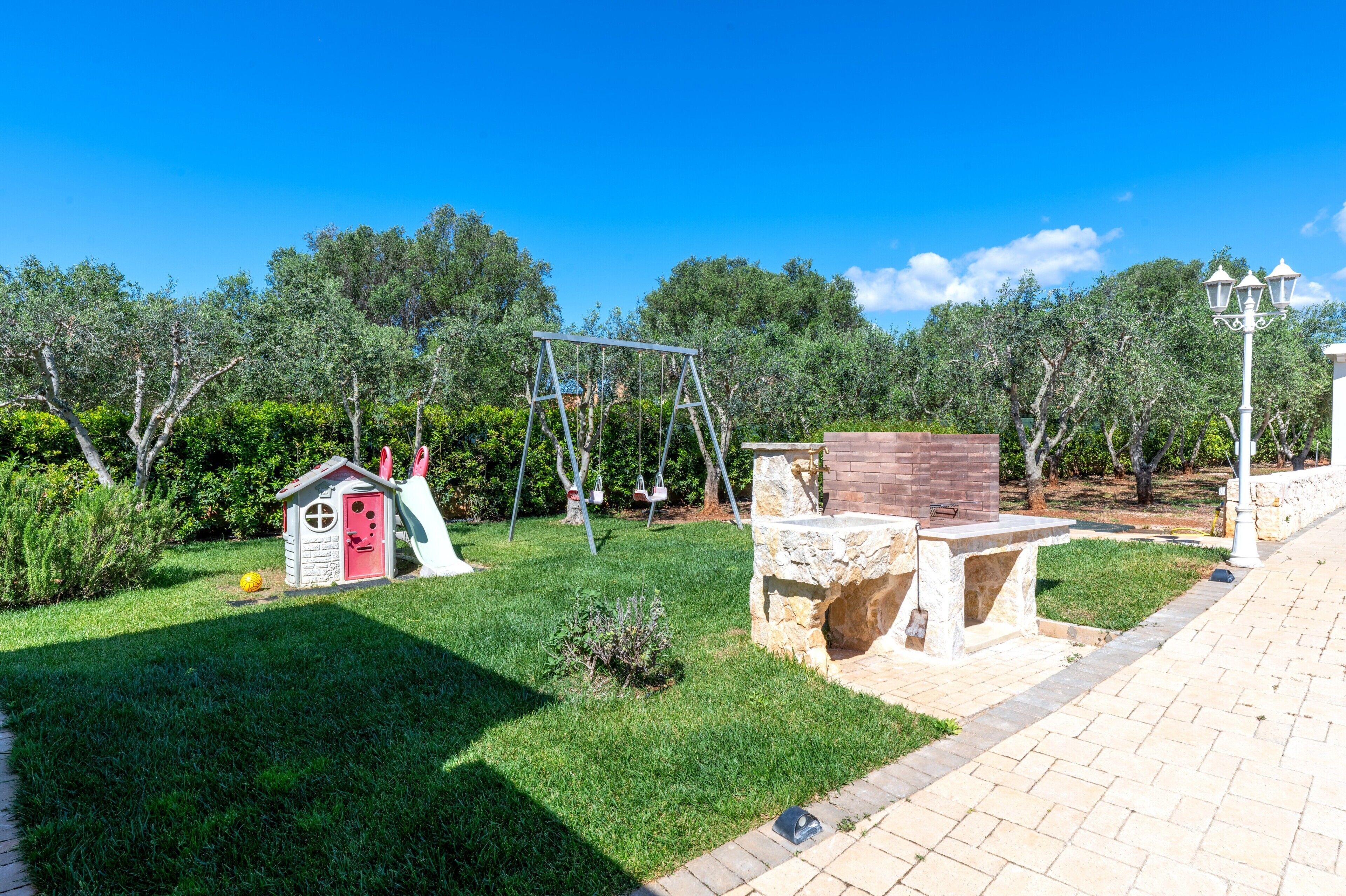 Un giardino con un'altalena, una casetta per bambini e una panchina in pietra.
