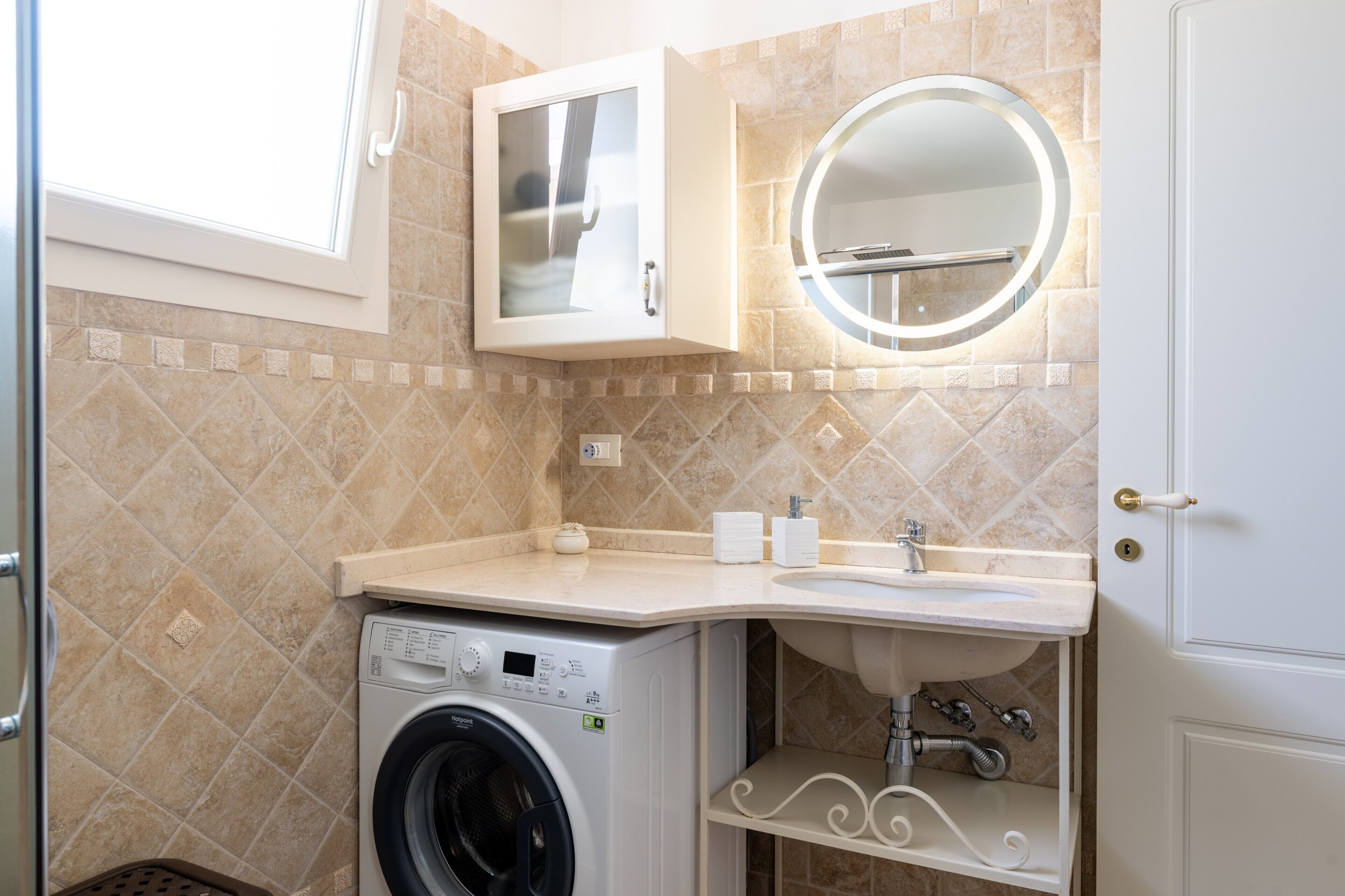 A compact bathroom with a washing machine, a sink, a mirror, and a cabinet.