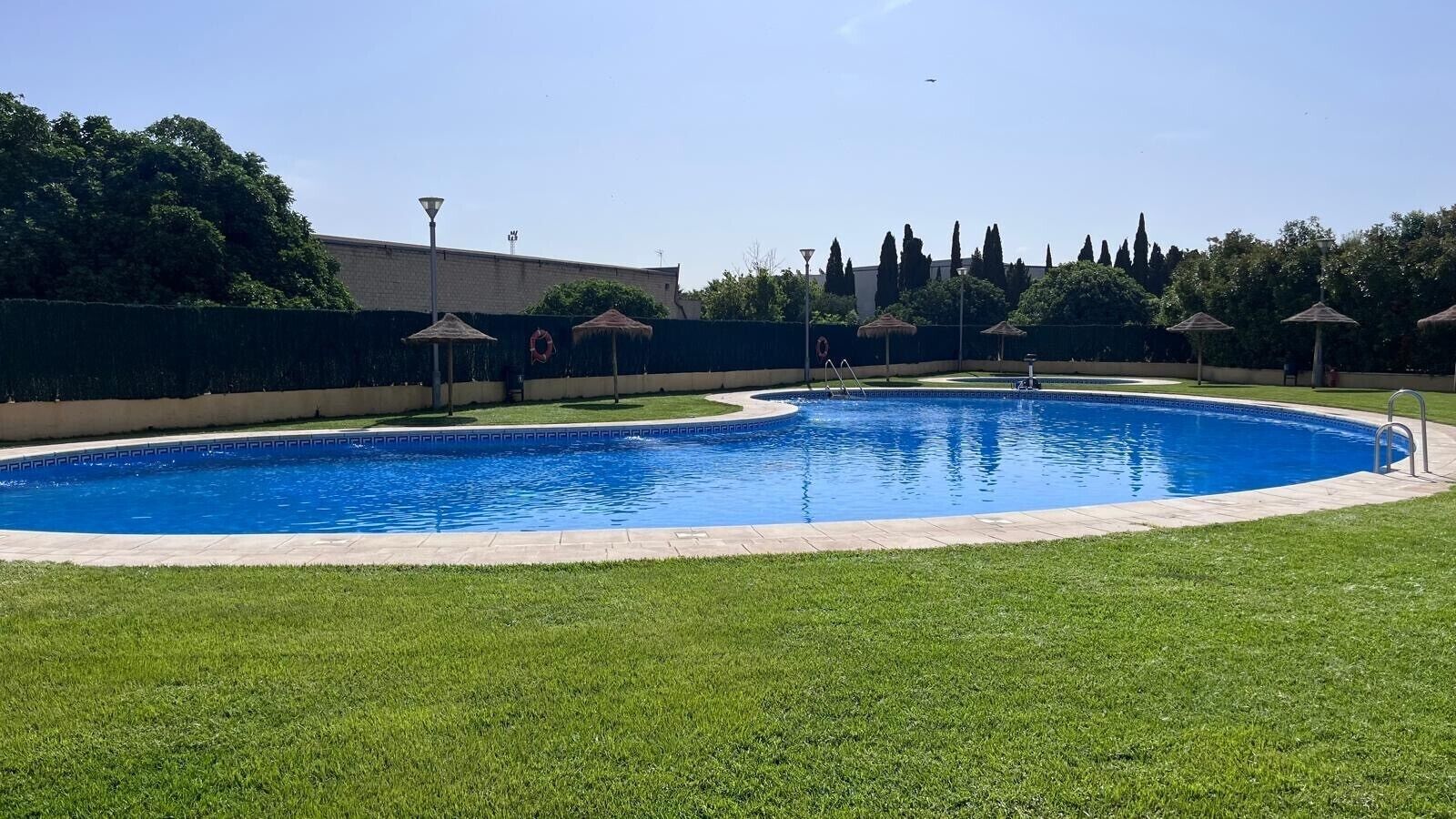 Una piscina con un área verde circundante y sombrillas.