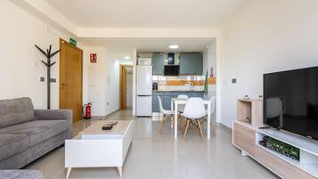Una sala moderna con un sofá, una mesa de centro, televisión y una cocina al fondo.