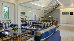 Amplia sala de estar con un gran sofá, una mesa de centro de vidrio y una escalera que conduce a un nivel superior.