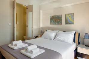 Habitación de hotel con cama, toallas, mesita de noche, lámpara y dos cuadros en la pared.