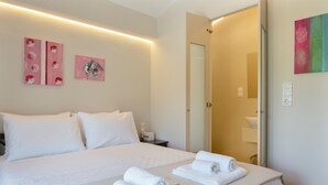 Habitación de hotel con una cama grande, dos cuadros en la pared, un baño con espejo y toallas ordenadas sobre la cama.