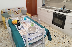 Een eethoek met een tafel gedekt voor twee personen, een keuken met een fornuis en oven, en een gestreept banksofa.