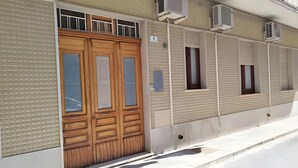 A building with a large wooden door, air conditioning units, and a number sign indicating the unit number.