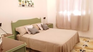 A bedroom with a green headboard, a beige bedspread, and a nightstand with a lamp.