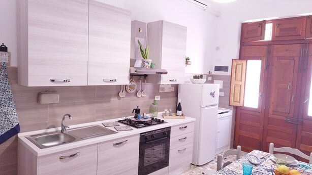 A modern kitchen with white cabinetry, a built-in oven, a sink, and a dining area with a table and chairs.