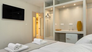 Hotellihuone, jossa on sänky, seinälle asennettu televisio, minijääkaappi, peili ja pyyhekoukku.