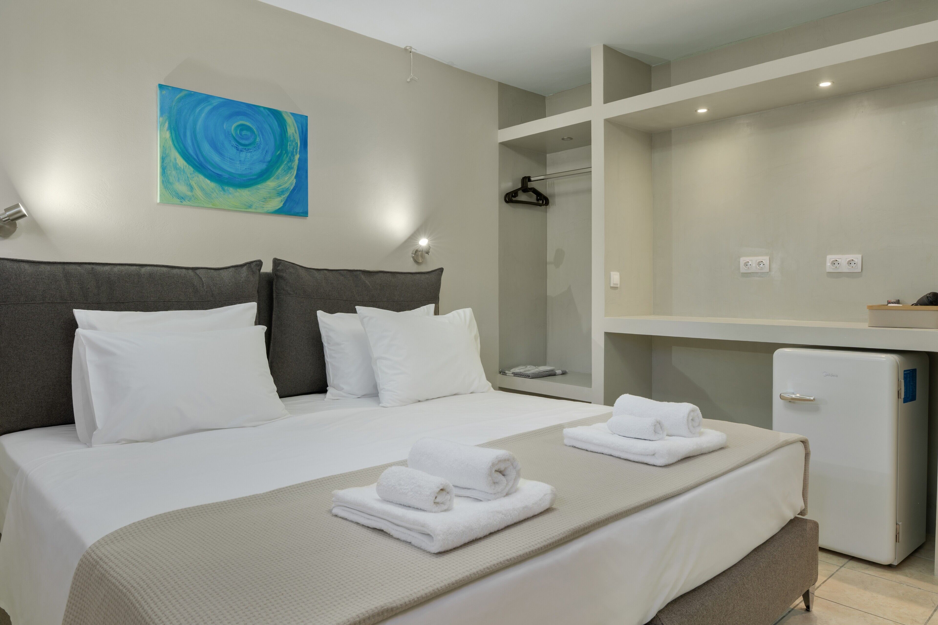 A hotel room with a bed, a small refrigerator, a bathroom, and a painting on the wall.